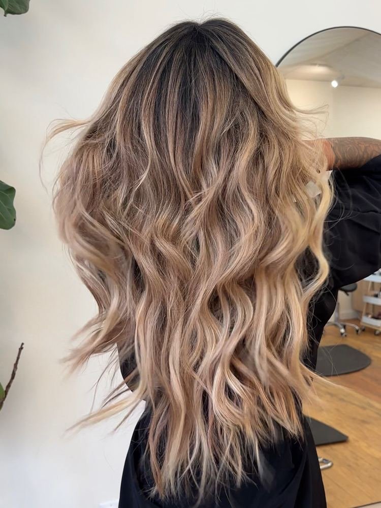 Back view of long, wavy blonde hair with a deeper root that blends into lighter, dimensional color through the lengths